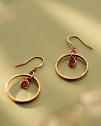 Pair of gold hoop earrings with red gemstones on a green background