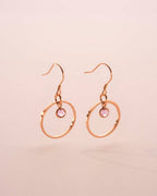 Gold hoop earrings with pink gemstones on a beige background