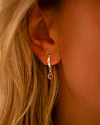 Close-up of an ear wearing a silver hoop earring with a heart-shaped gemstone. | Christmas