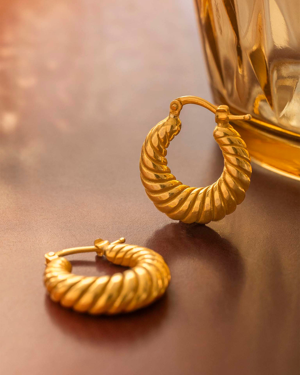 Gold hoop earrings on a reflective surface with a blurred background