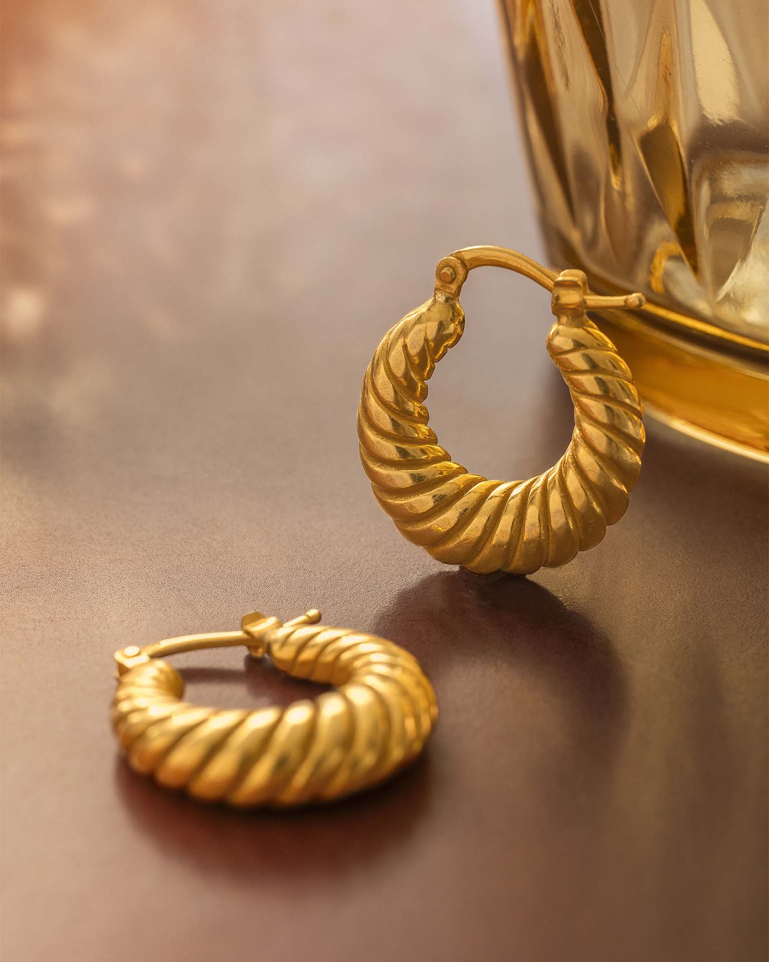 Gold hoop earrings on a reflective surface with a blurred background