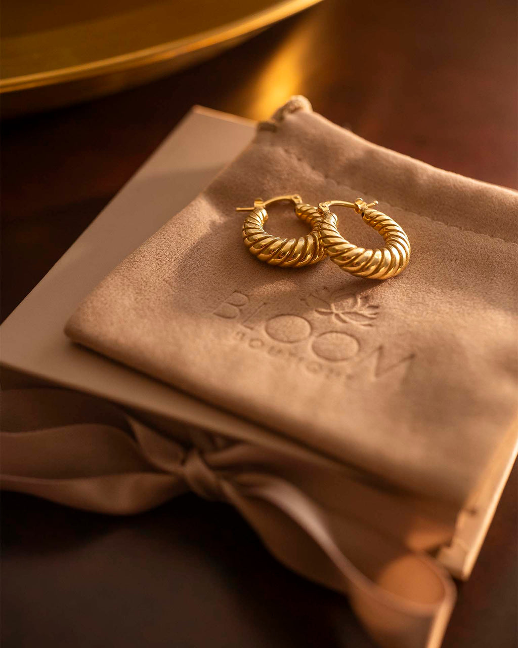 Gold hoop earrings on a beige pillow with 'BLOOM' branding.