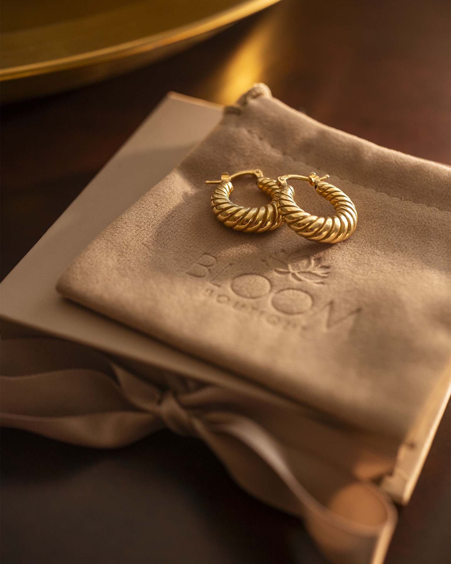 Gold hoop earrings on a beige pillow with 'BLOOM' branding.