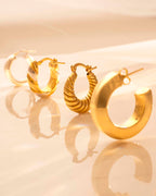 Set of gold hoop earrings on a reflective surface with a beige background