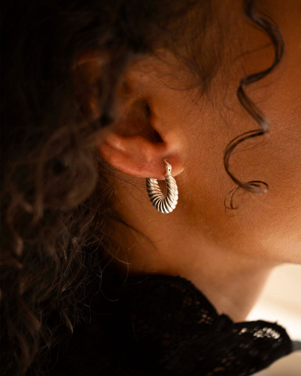 Close-up of an ear wearing a gold hoop earring with soft lighting.