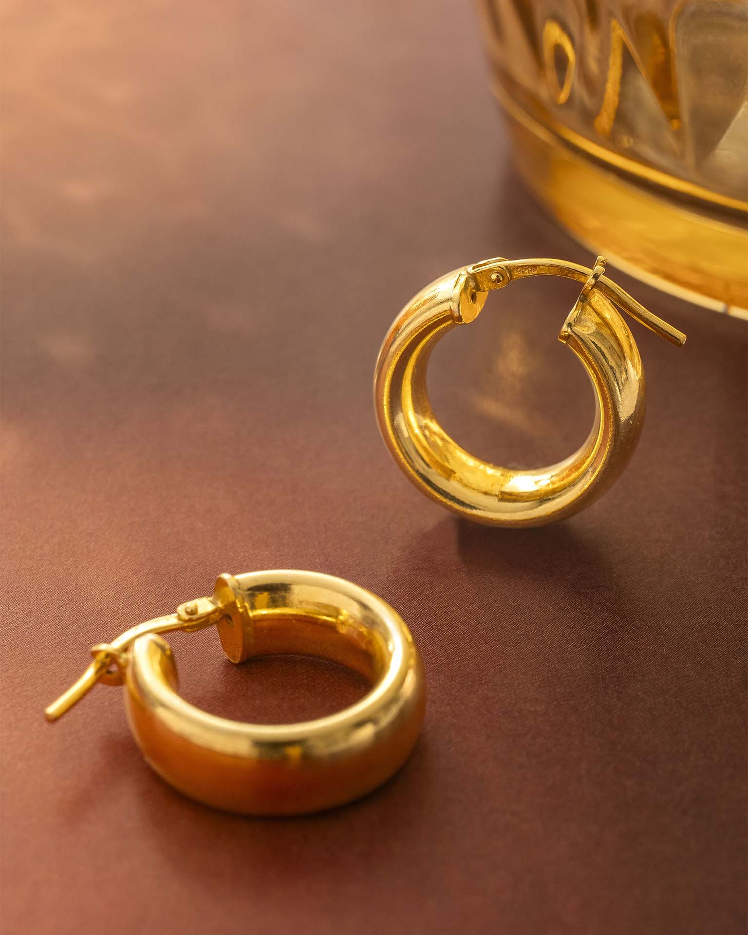 Gold hoop earrings on a reflective surface with a blurred background | Christmas