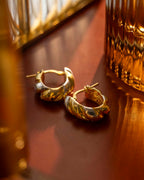 Gold hoop earrings on a reflective surface with a blurred background  | Christmas