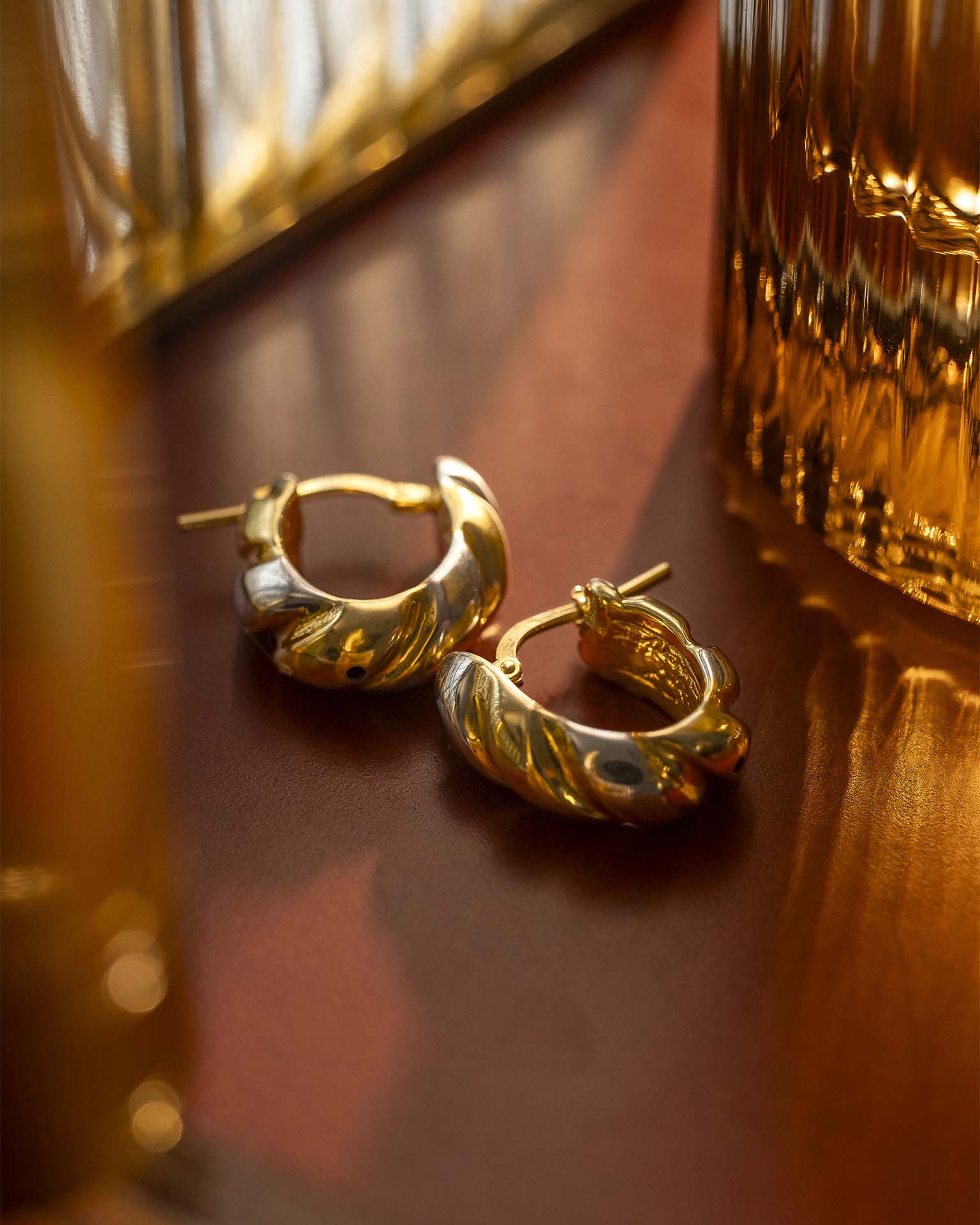 Gold hoop earrings on a reflective surface with a blurred background  | Christmas