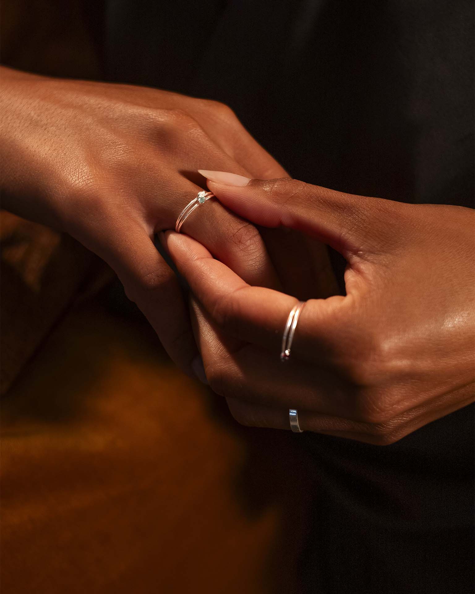 Close-up of two hands with silver rings on a dark background