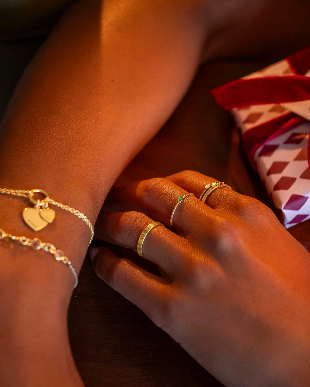Close-up of hands wearing gold rings and bracelets with a gift box in the background.