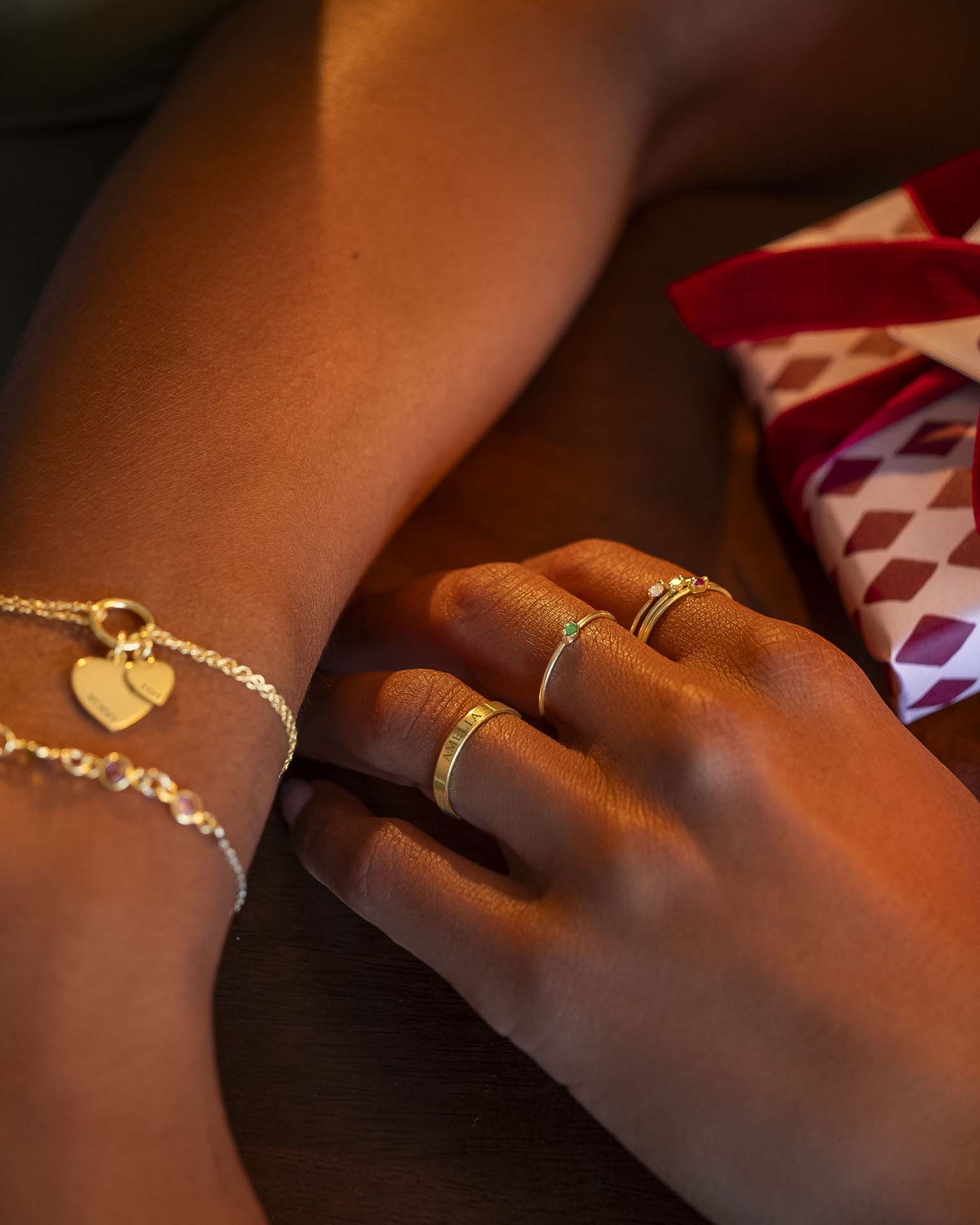Close-up of hands wearing gold rings and bracelets with a gift box in the background.