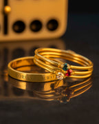 Three gold rings with engraved text and gemstones on a reflective surface.