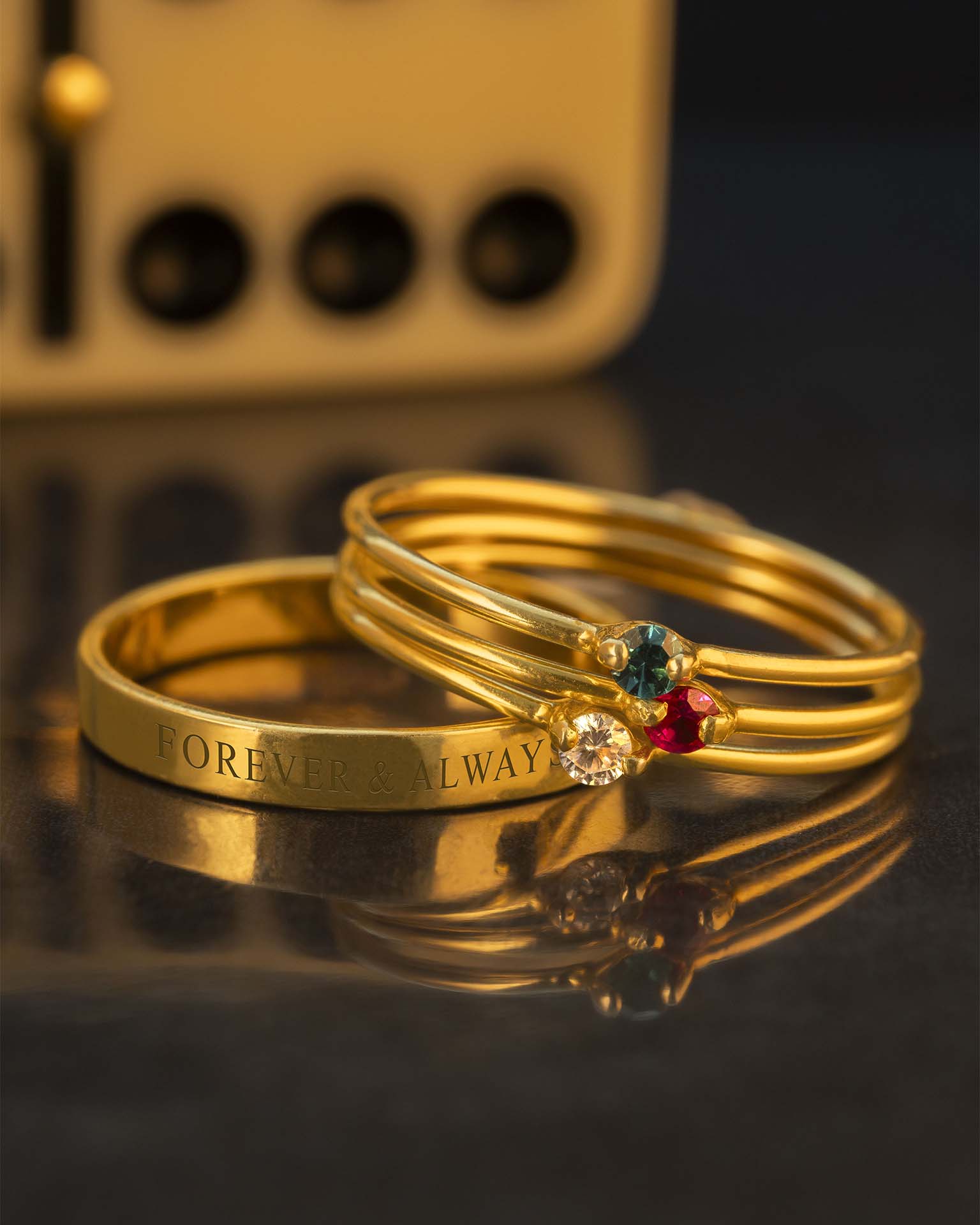 Three gold rings with engraved text and gemstones on a reflective surface.