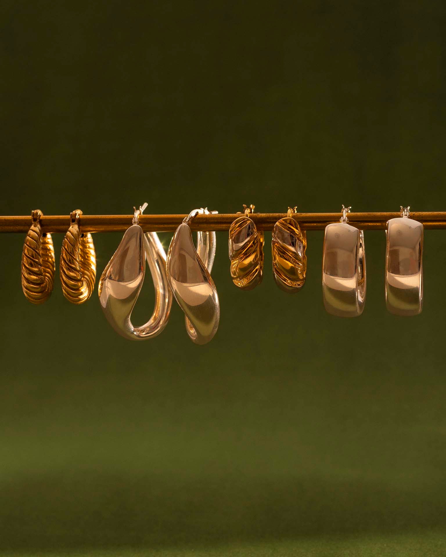 Set of gold and rose gold hoop earrings on a dark green background