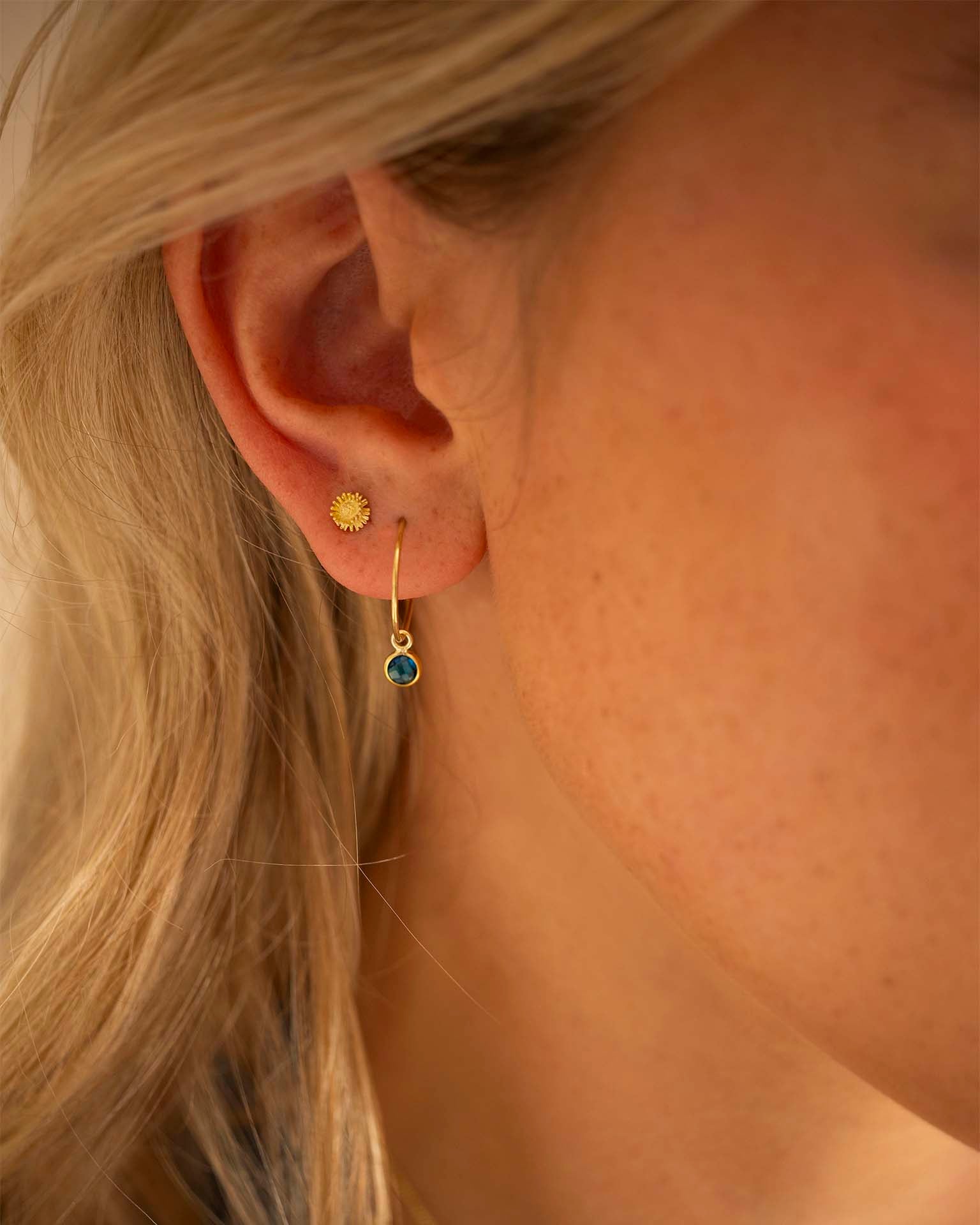 Close-up of an ear wearing gold earrings with a blue gemstone.