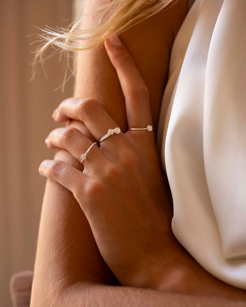 Close-up of a person wearing multiple delicate rings on a soft background