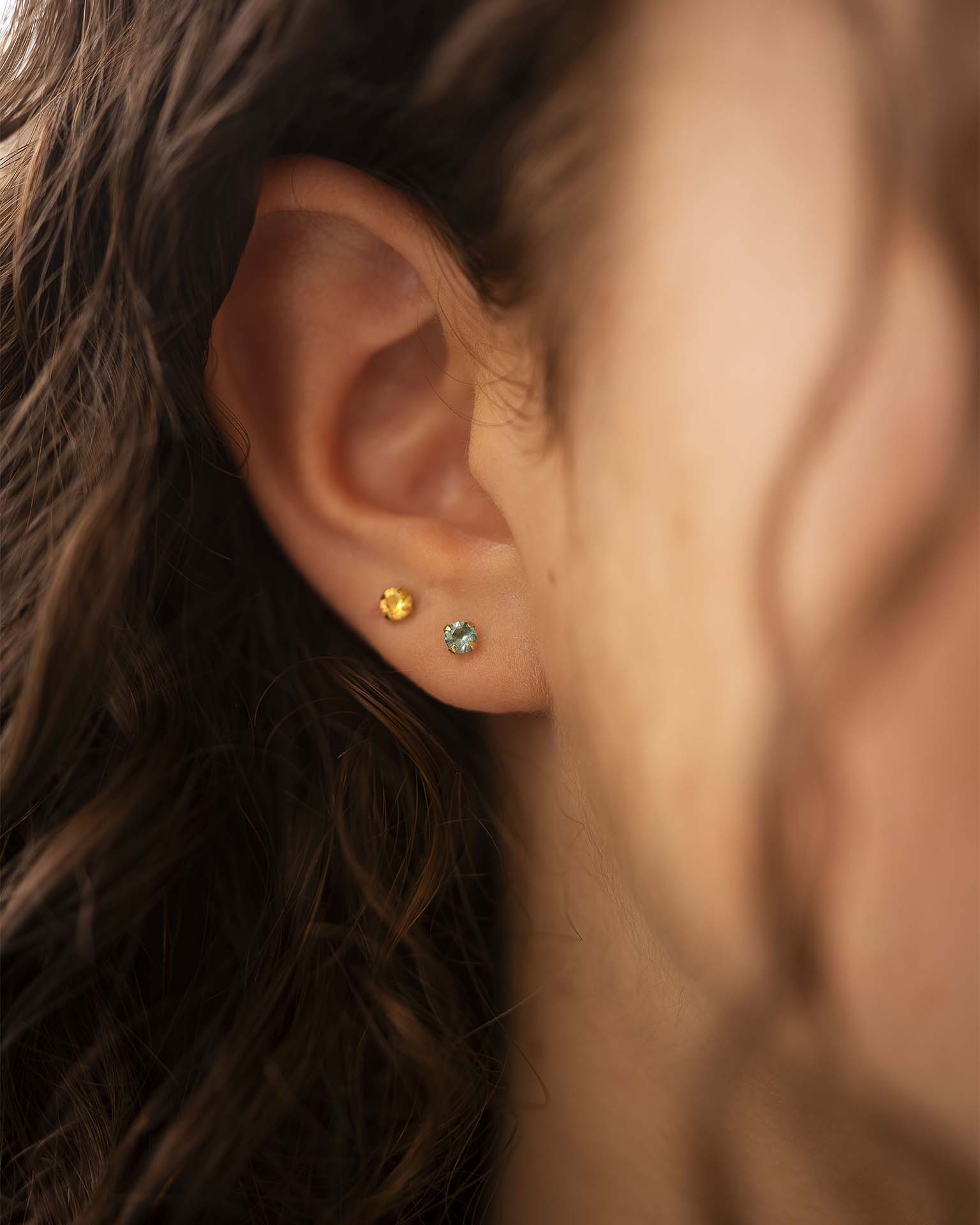 Close-up of an ear wearing two small stud earrings with a blurred background