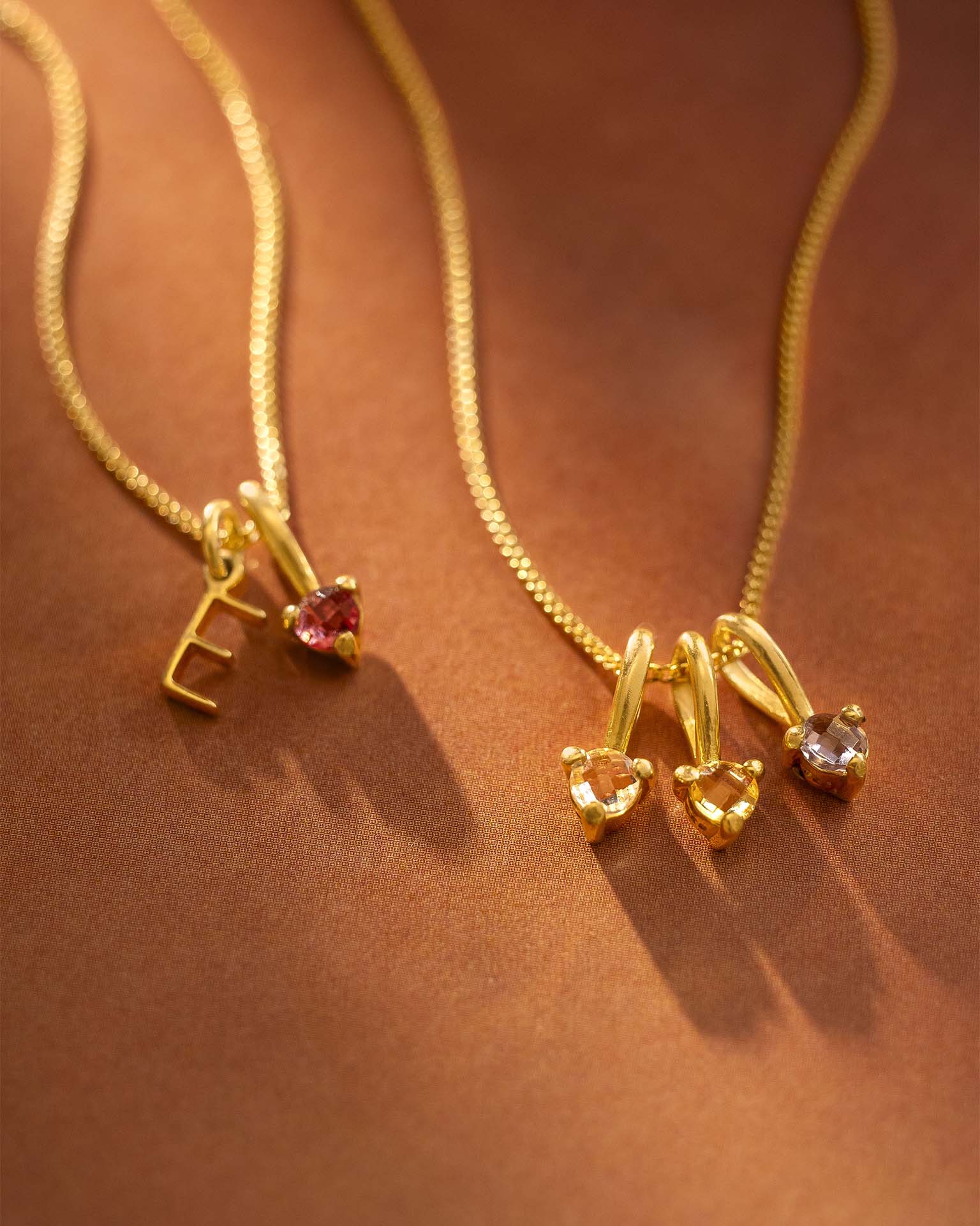 Two gold necklaces with gemstone pendants on a brown background