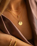 Gold necklaces and bracelet on a person against a brown fabric background