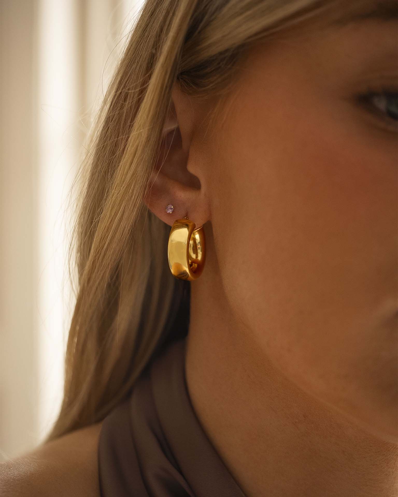 Close-up of a person wearing gold hoop earrings with a neutral background