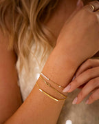 Close-up of a person's wrist wearing gold bracelets with a neutral background
