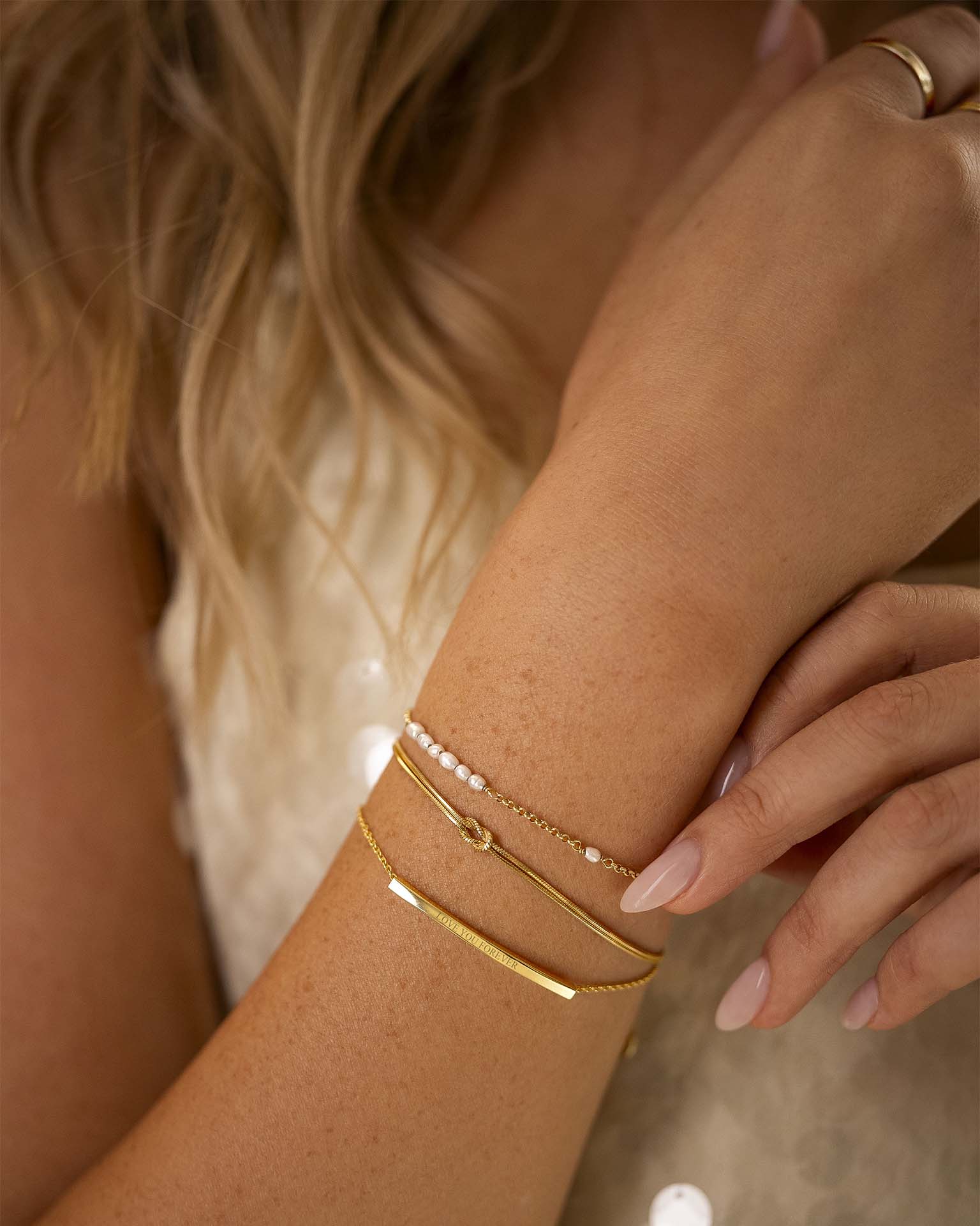 Close-up of a person's wrist wearing gold bracelets with a neutral background