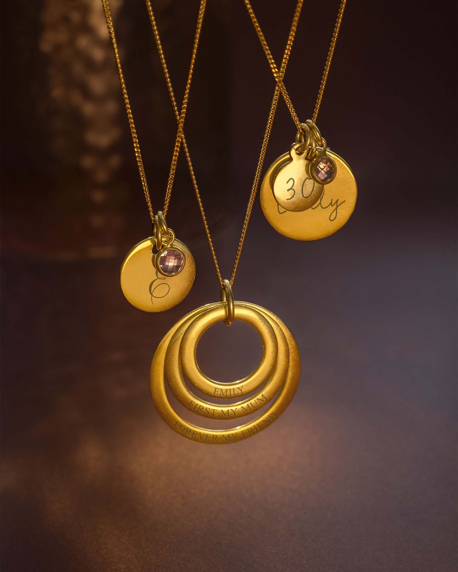 Three gold necklaces with circular pendants on a dark background
