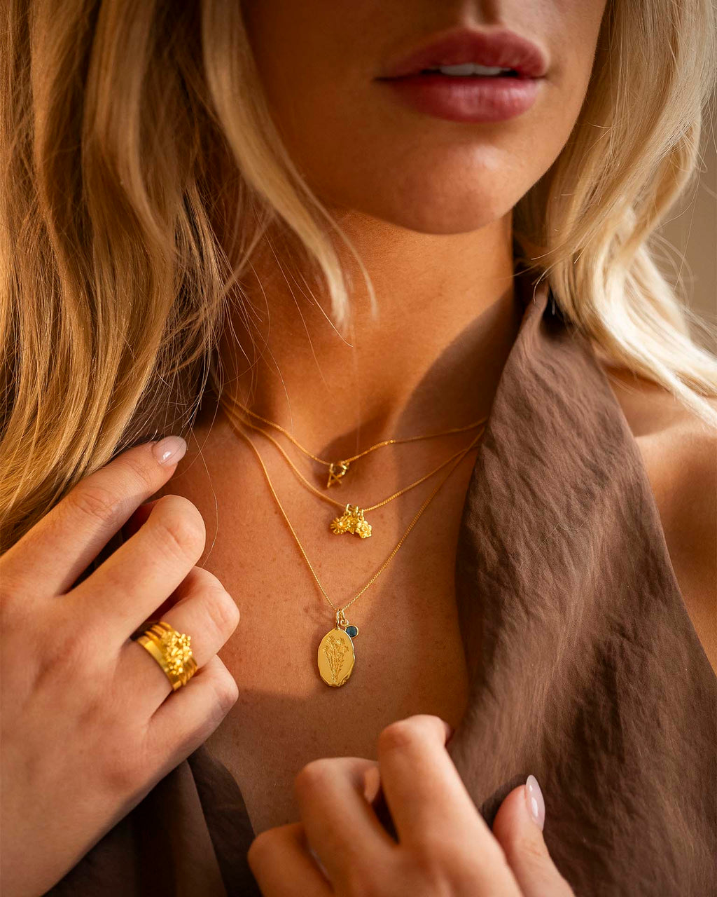 Close-up of a woman wearing gold necklaces and rings with a neutral background