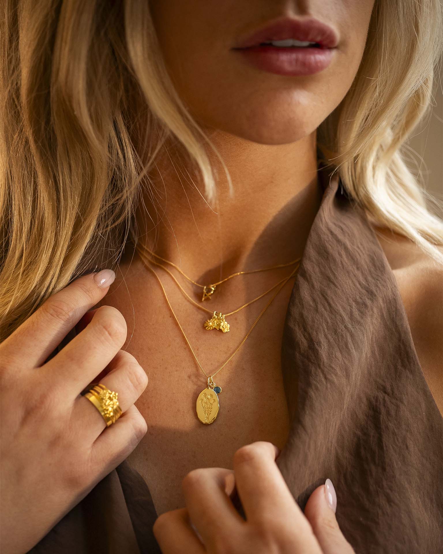 Close-up of a woman wearing gold necklaces and rings with a neutral background