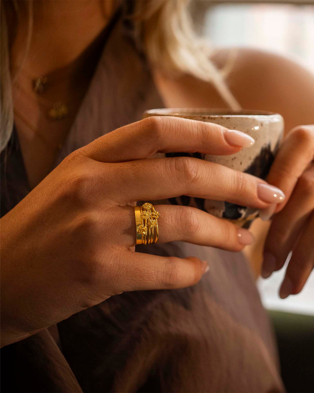 Close-up of a hand holding a mug with a gold ring on a blurred background