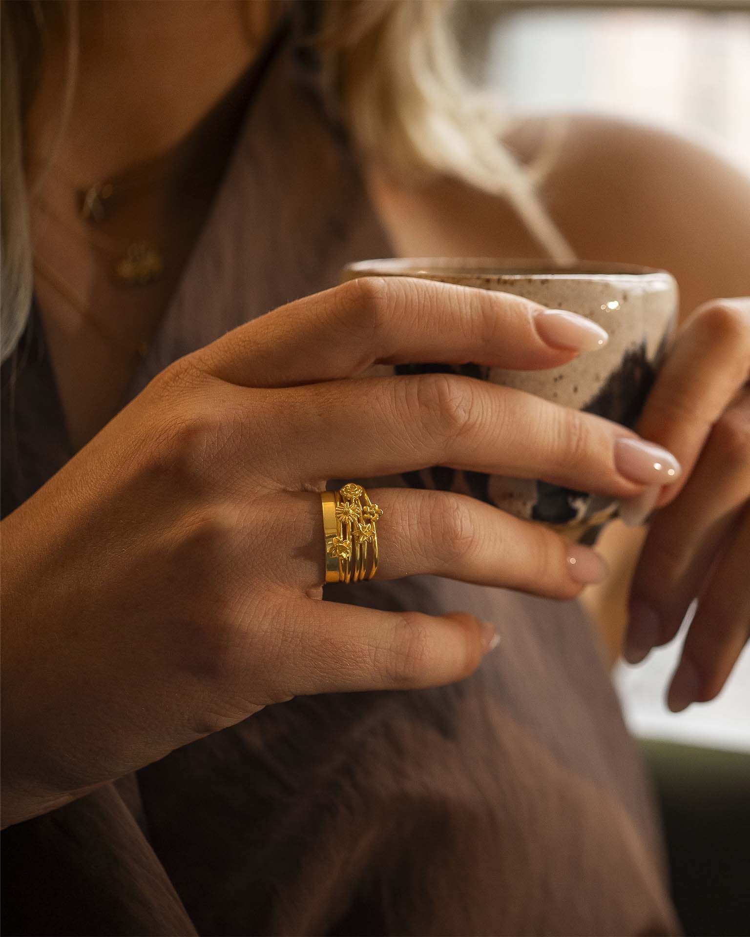 Close-up of a hand holding a mug with a gold ring on a blurred background