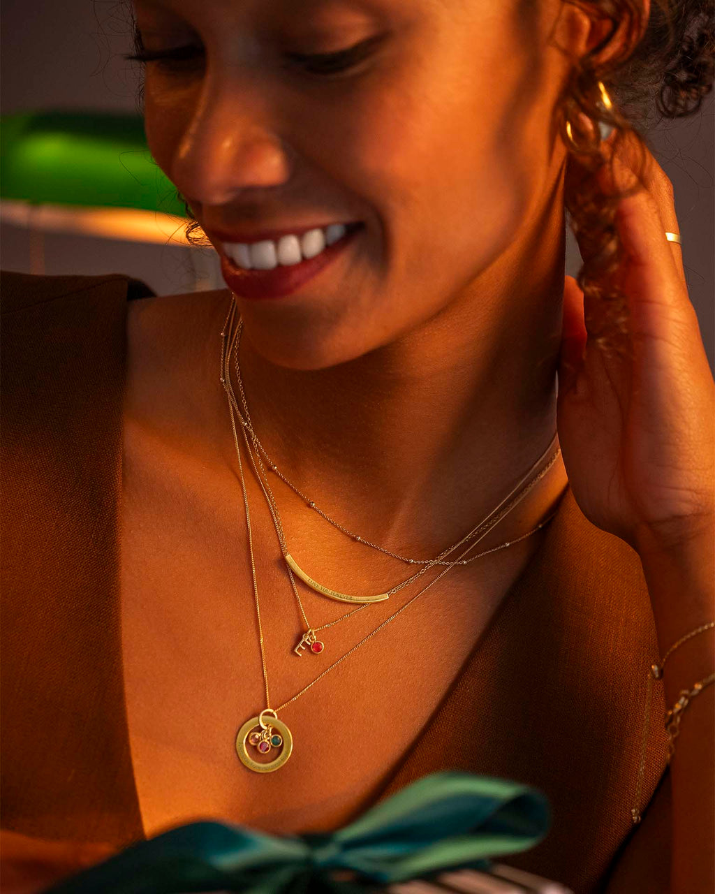 Woman wearing gold jewelry, including a necklace and earrings, with a blurred background.