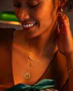 Woman wearing gold jewelry, including a necklace and earrings, with a blurred background.