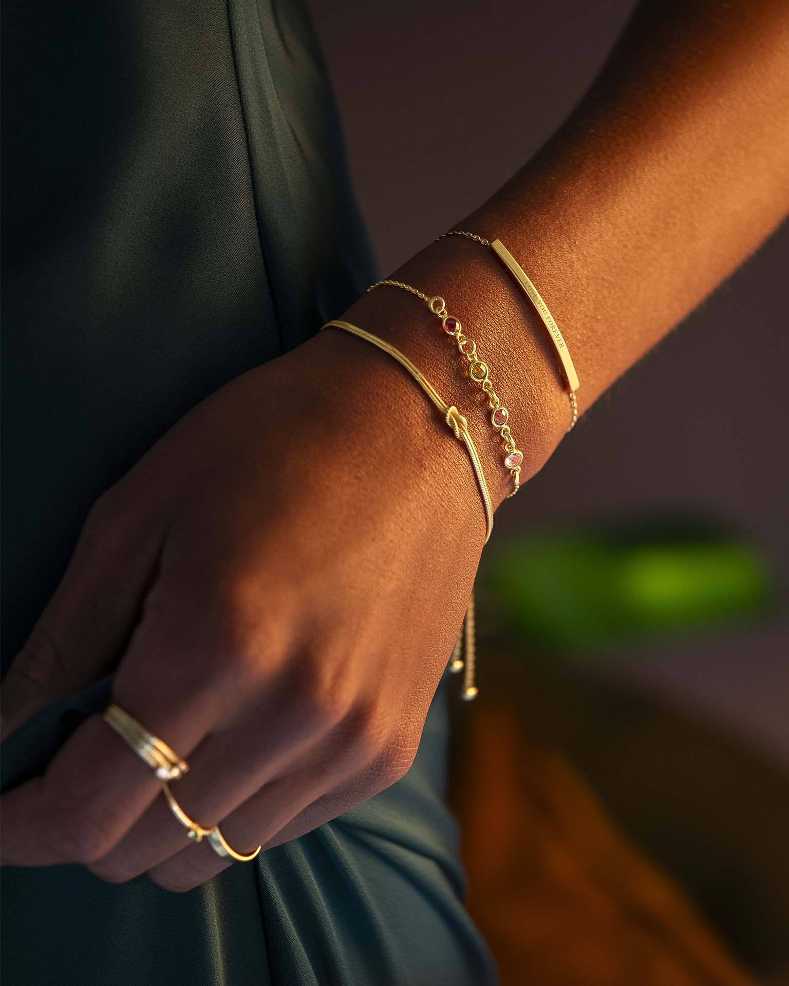 Close-up of a hand wearing gold bracelets and rings against a blurred background