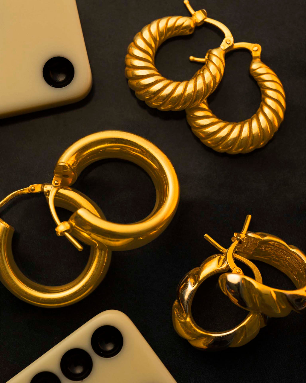 Gold hoop earrings on a dark surface with smartphone and remote control.