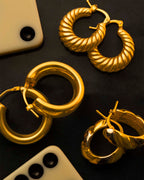 Gold hoop earrings on a dark surface with smartphone and remote control.
