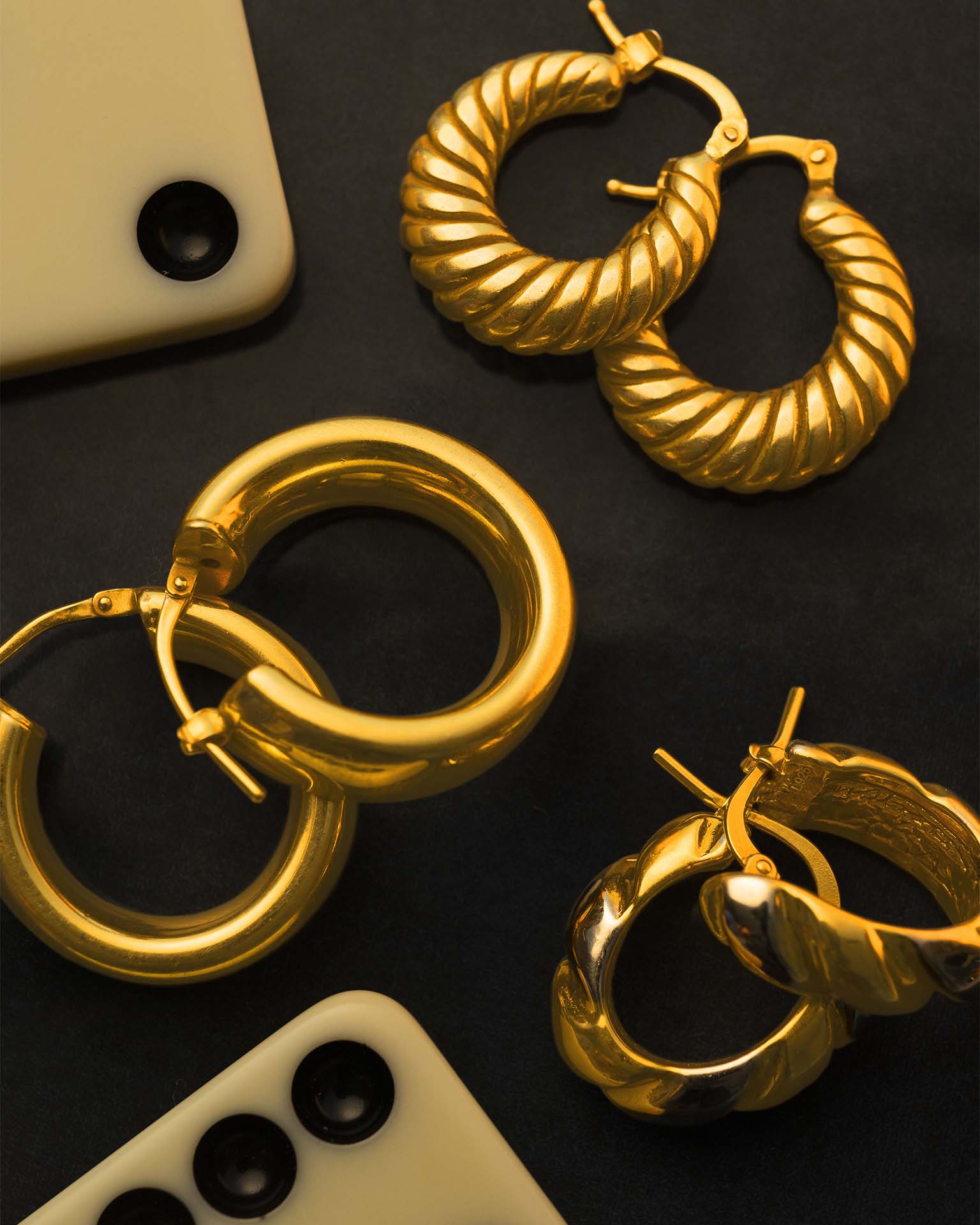 Gold hoop earrings on a dark surface with smartphone and remote control.