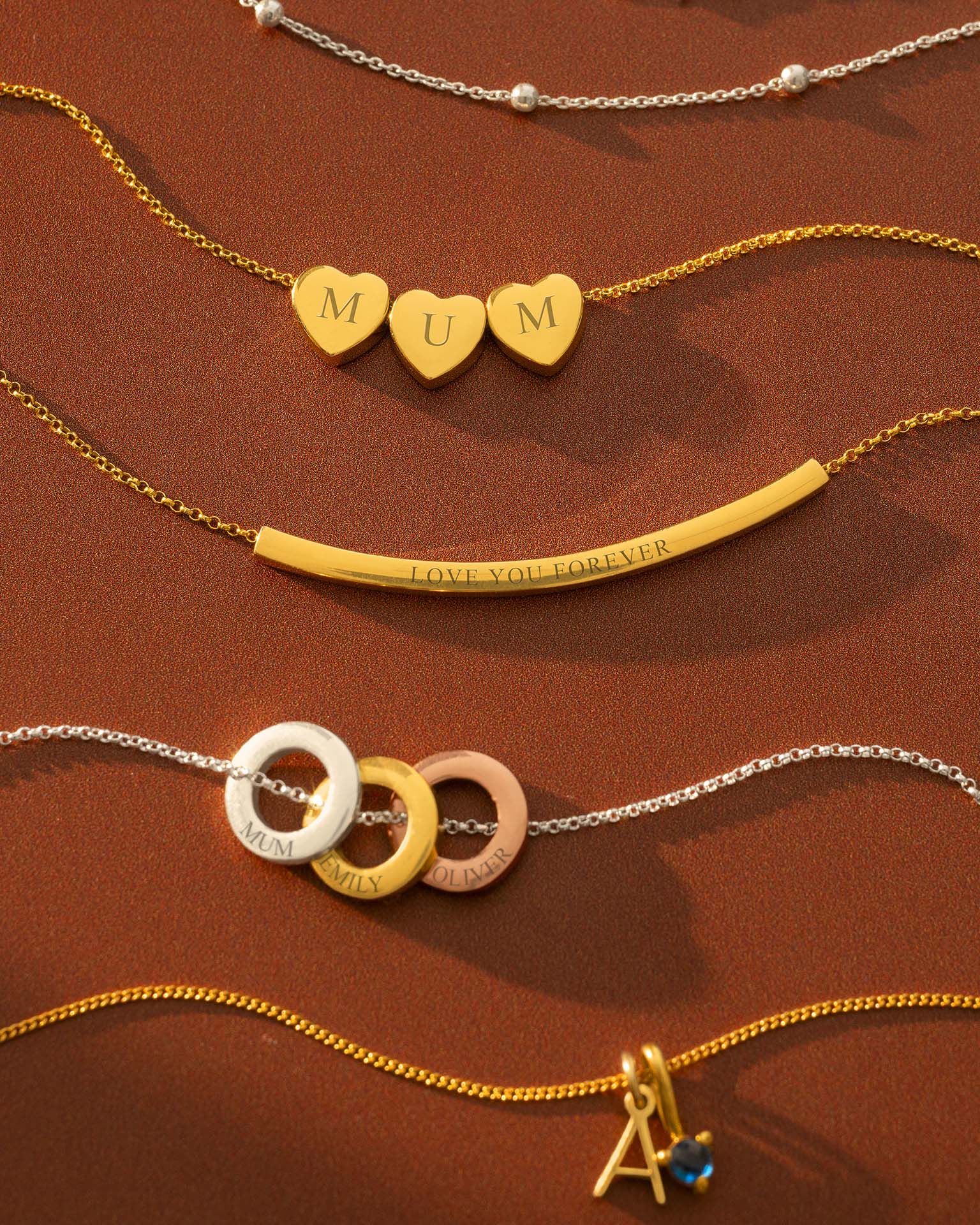 Collection of gold and silver necklaces with heart-shaped pendants and engraved text on a brown background.