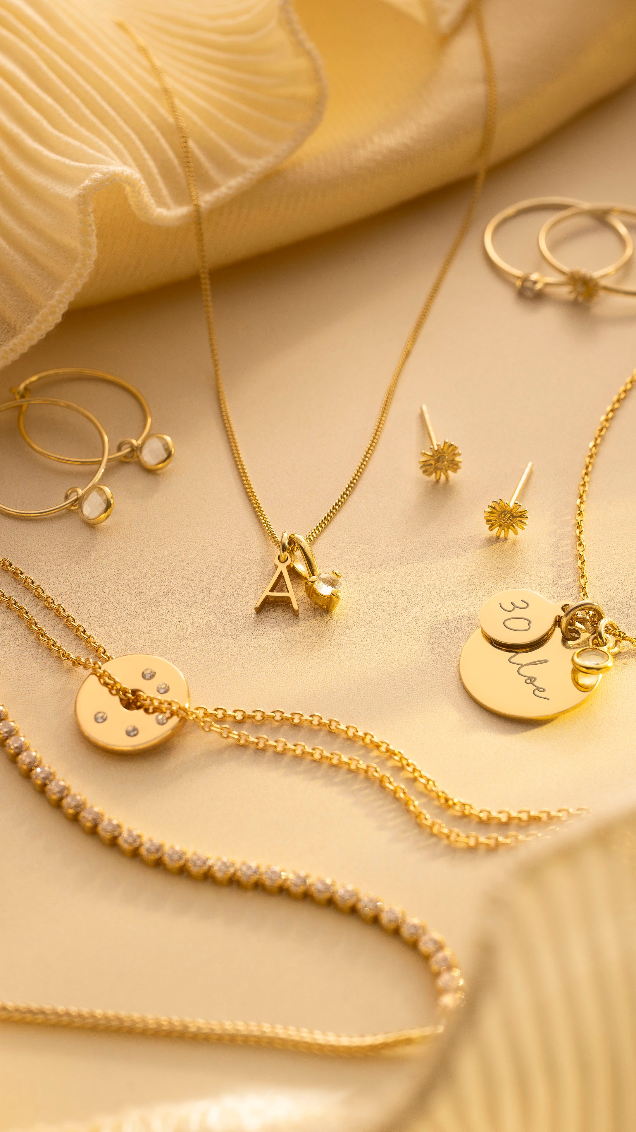 Collection of gold jewelry including necklaces and earrings on a beige fabric background