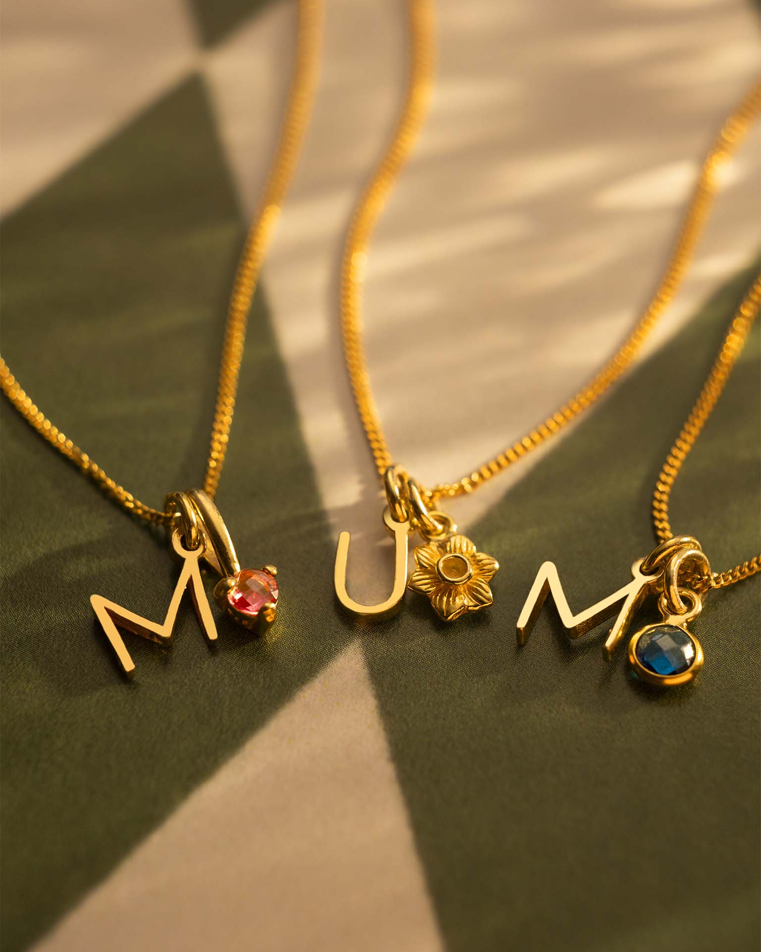 Three gold necklaces with charms on a textured surface