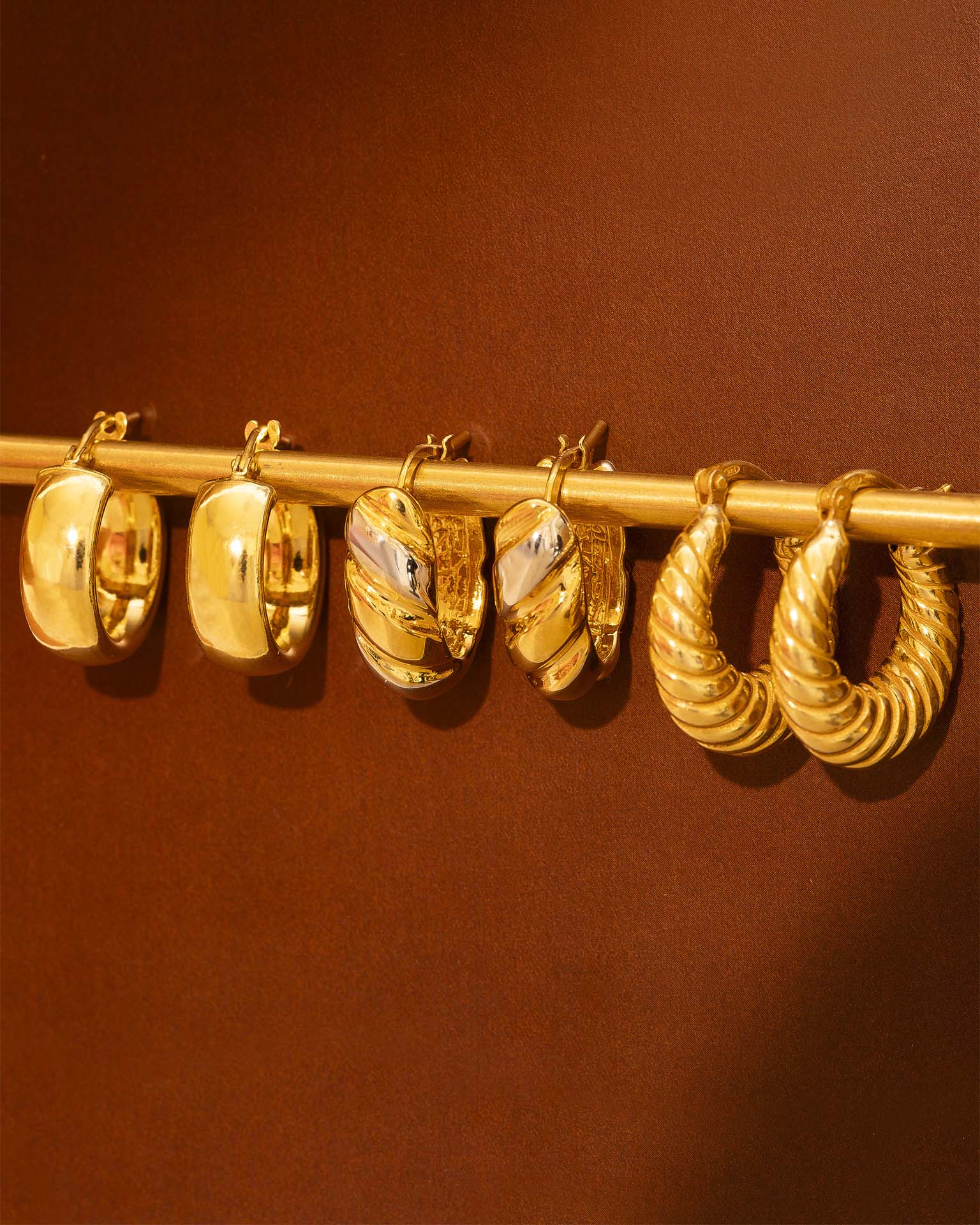 Set of gold hoop earrings on a rod against a brown background