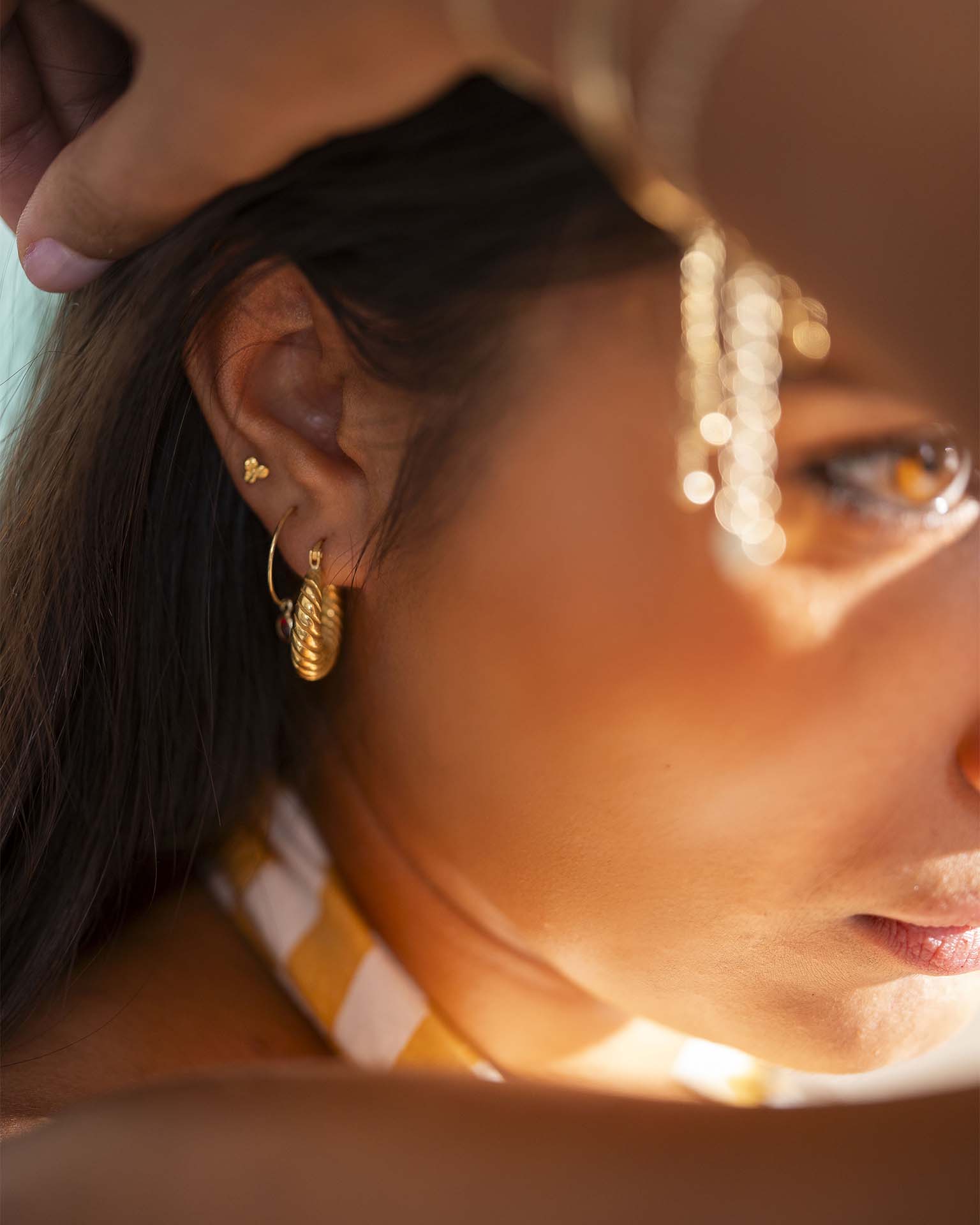 Close-up of a woman wearing gold hoop earrings with a blurred background