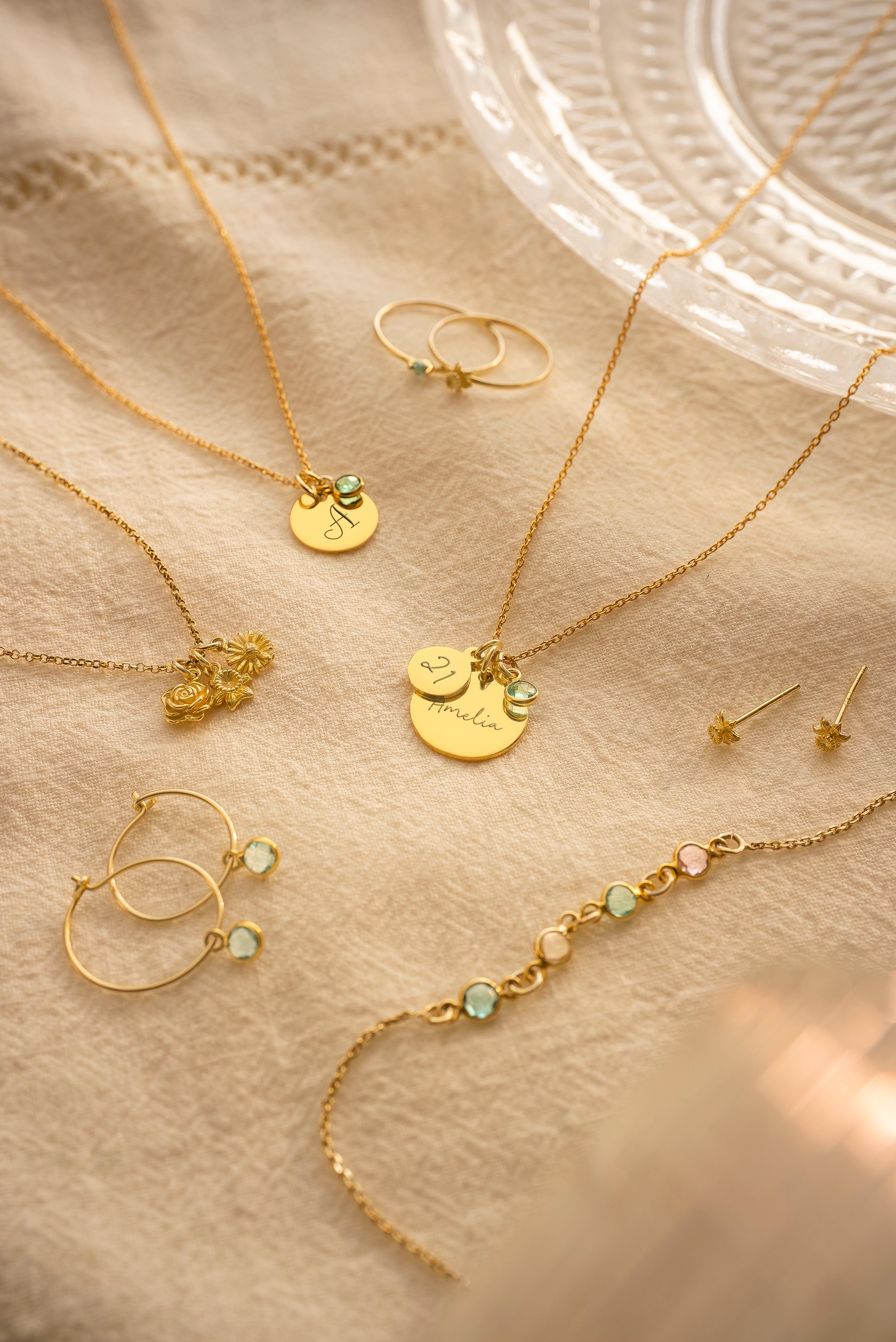 Gold jewelry including necklaces, earrings, and rings on a beige surface.