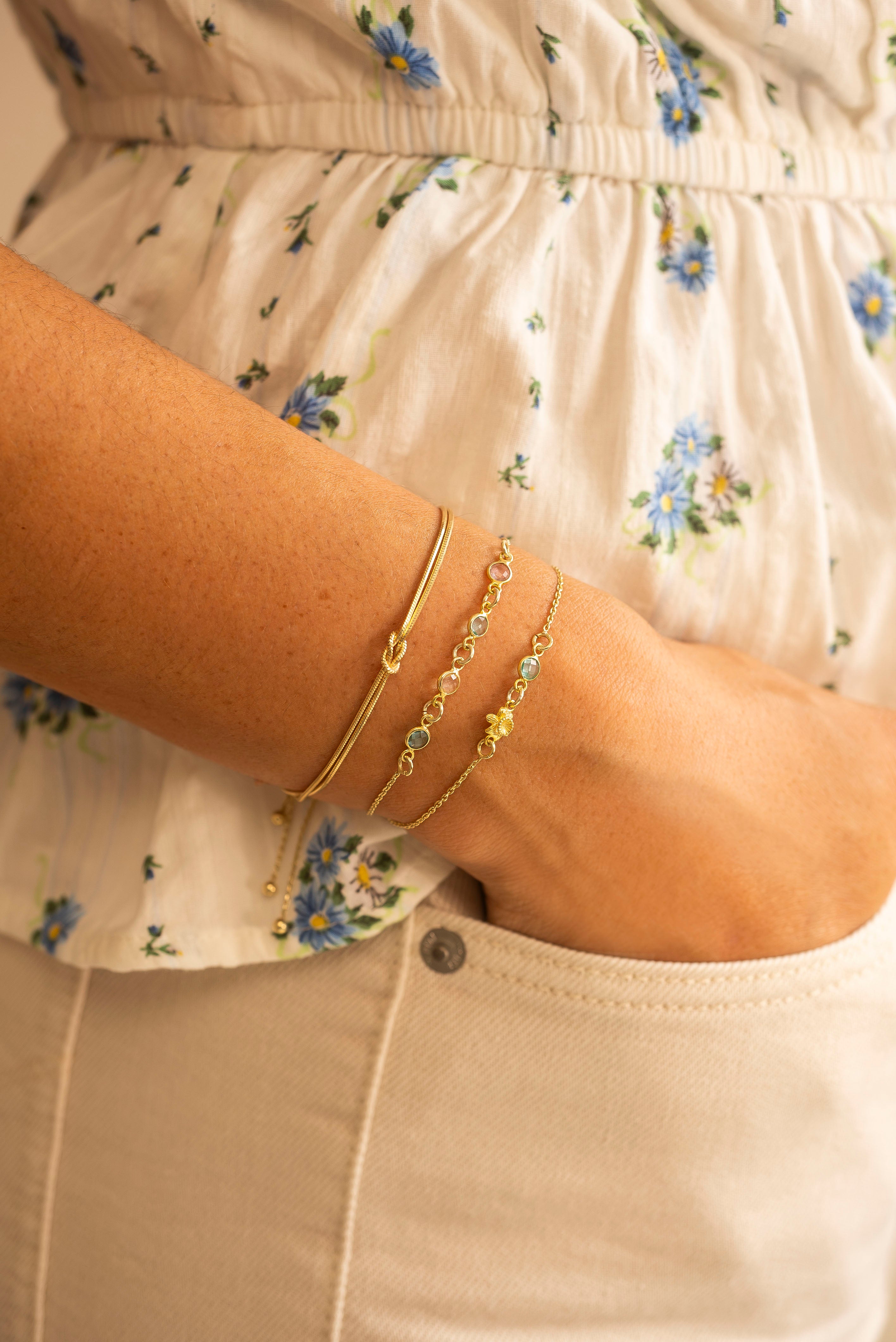 Close-up of a person's arm wearing gold bracelets on a floral shirt background