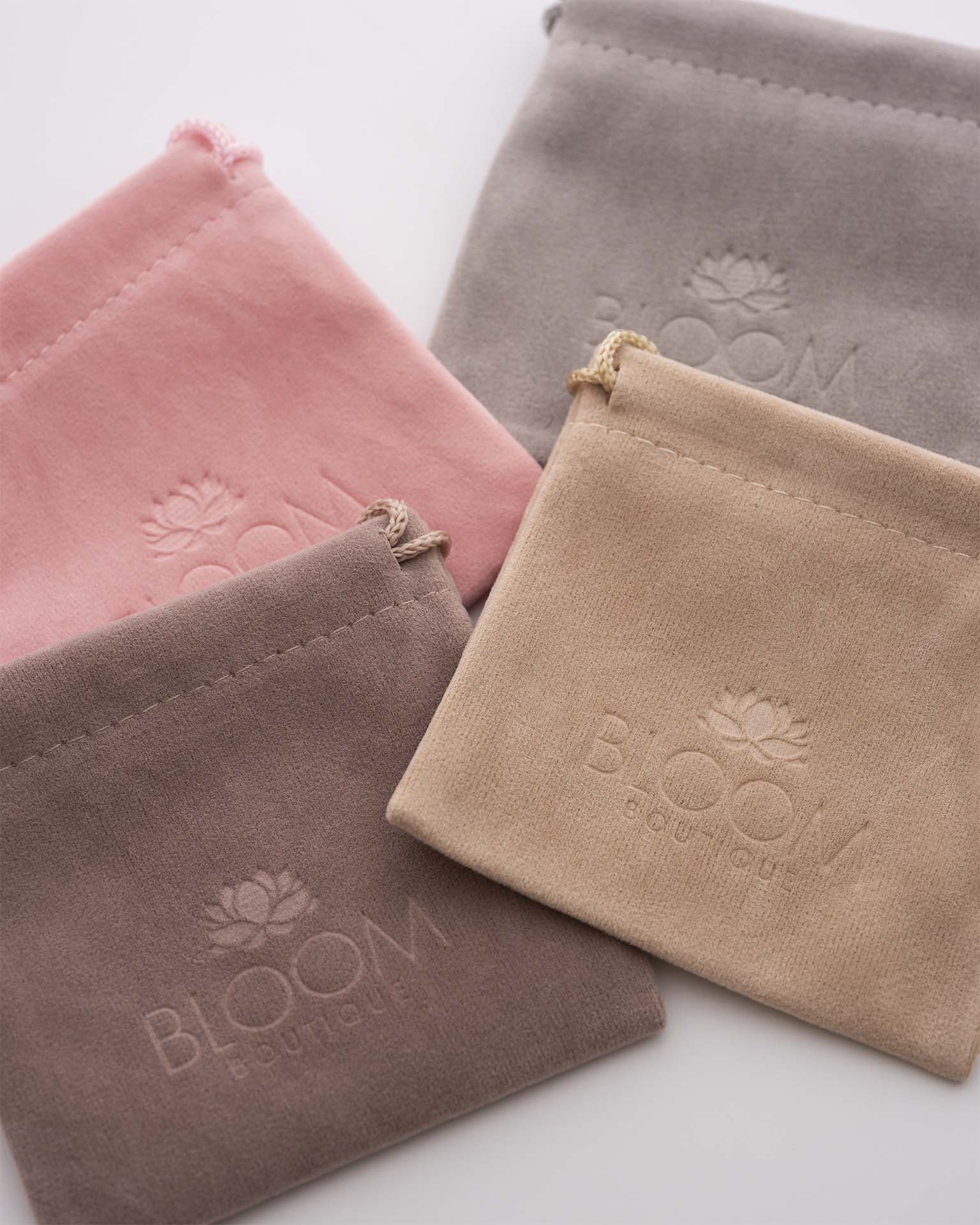 Four suede pouches in pink, gray, and brown with 'Bloom' branding on a light background.