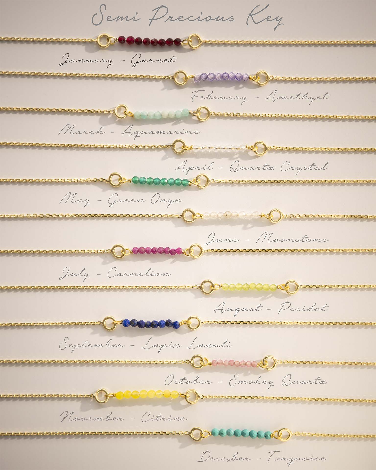 Set of gold bracelets with colored beads for each month, on a light background.