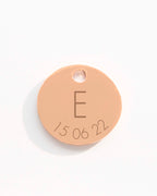Round beige metal tag with letter 'E' and numbers '15 06 22'