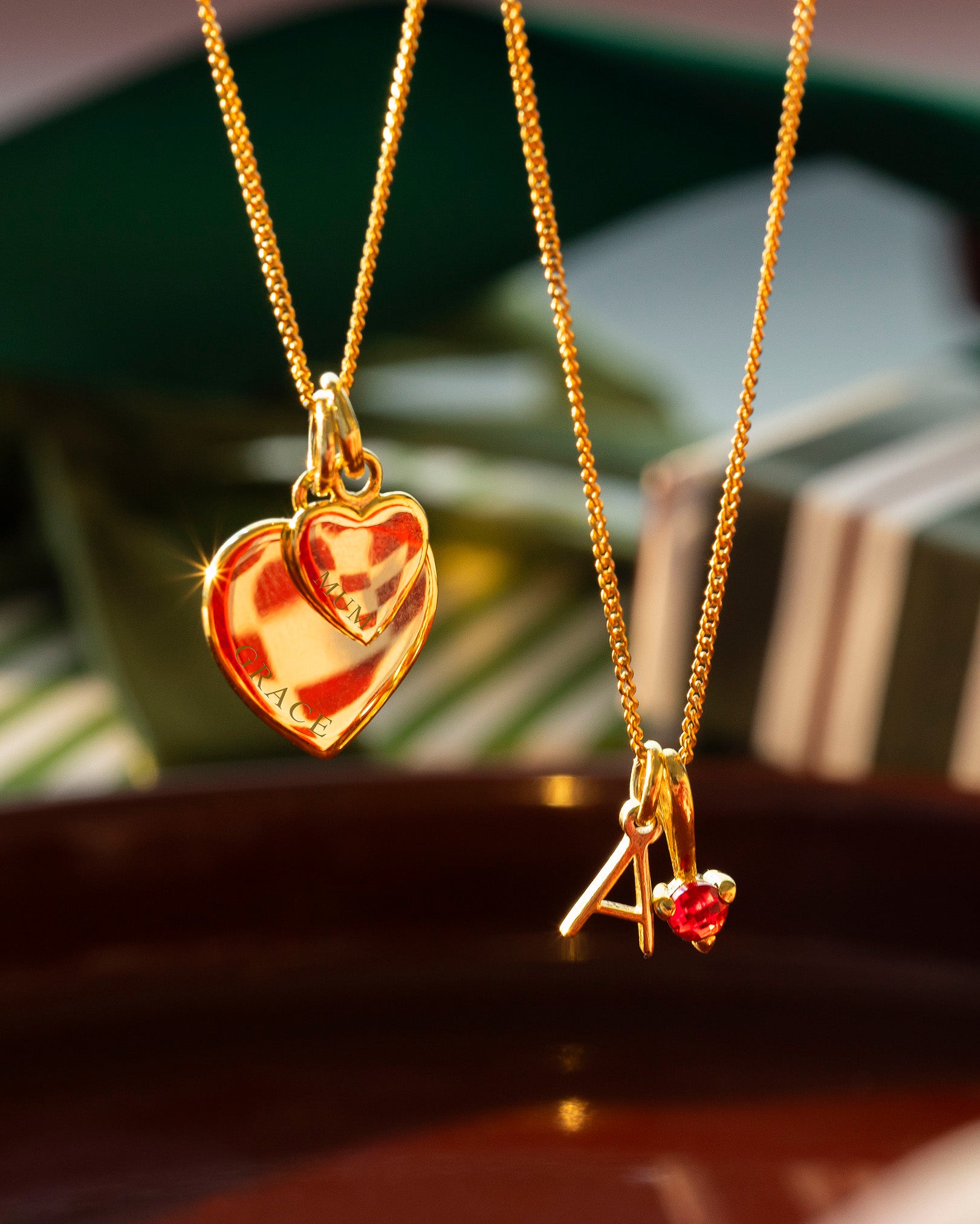 Two gold necklaces with heart and letter 'A' pendants on a wooden surface.