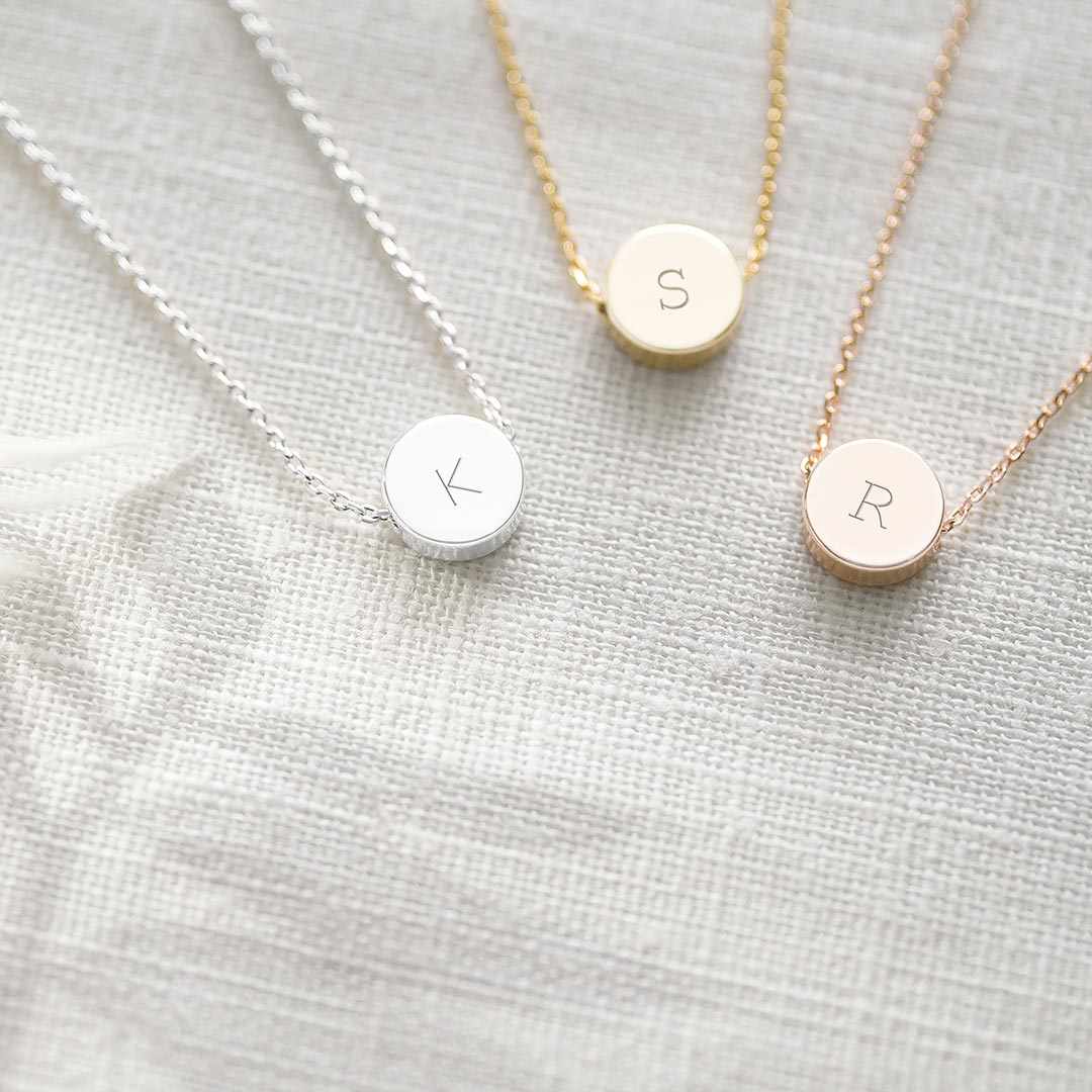 a slide-on disc charm seated atop of a trace chain personalised with an initial in a variety of fonts, available in three colourways.